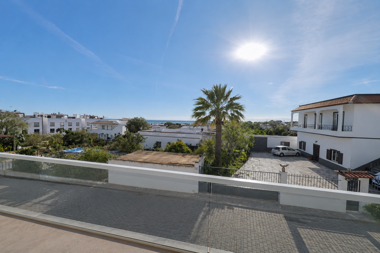 Vue depuis la terrasse — palmier, toits blancs et mer à l'horizon